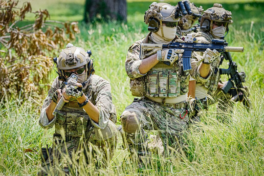 Special forces soldiers in camouflage gear aiming rifles in tall grass