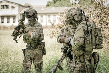 Fototapeta premium Special forces soldiers in camouflage gear with rifles stand in a grassy field