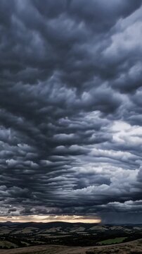 Dark storm clouds rolling over hills, massive cumulonimbus layers churn above patchwork fields at dusk, low light accentuates turbulent textures and deep contrast storm chaser drone documents approach