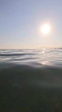 Vertical view of calm ocean surface under a bright sun, beautiful and soft golden hour light, horizon line, creating a peaceful and serene seascape