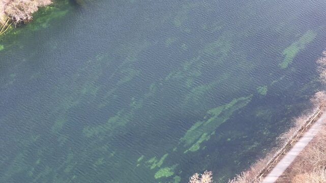 Aerial view of clear river water with green underwater patterns along shoreline