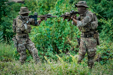 Fototapeta premium Two soldiers in camouflage gear aiming rifles in a dense green forest setting