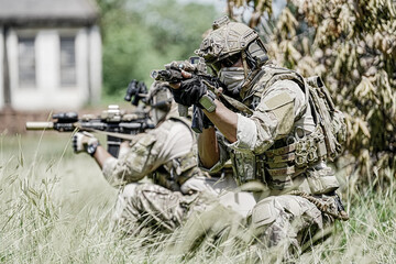 Fototapeta premium Special forces soldiers in camouflage gear aiming rifles in a grassy field