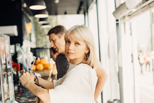 An adult mature happy couple in love in a street cafe order coffee. A blonde caucasian man and woman spend time together. Senior wife and husband walking outdoors