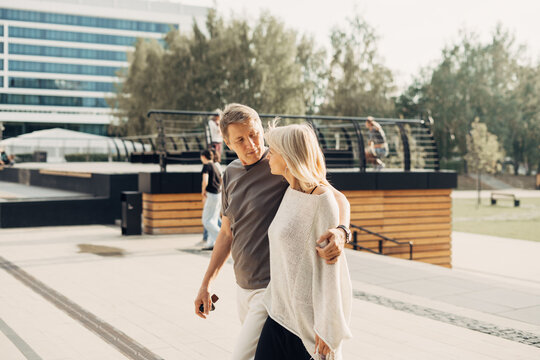 An adult mature happy romantic couple in love outdoors in city street park. A blonde caucasian man and woman spend time together. Senior wife and husband walking outside on town square