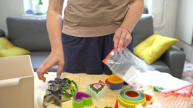 A woman organizes various cookie cutters and baking tools on a countertop in a bright and inviting kitchen. Her focus shows enthusiasm for baking during the afternoon.