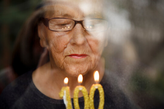 Portrait of an elderly woman with glasses holding anniversary candles.  An old woman holds a birthday cake alone on her centenary.