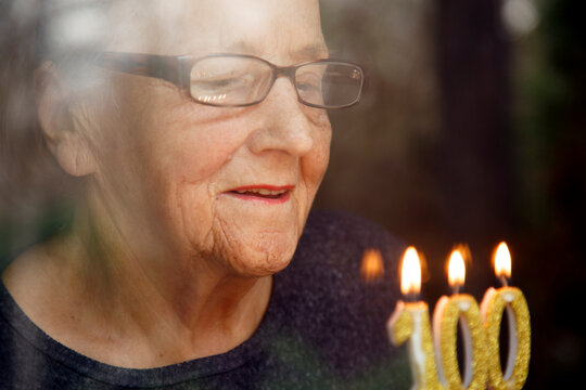 Portrait of an elderly woman with glasses holding anniversary candles.  An old woman holds a birthday cake alone on her centenary.