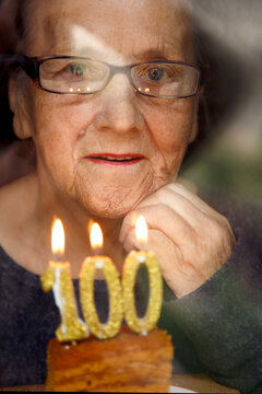 Portrait of an elderly woman with glasses holding anniversary candles.  An old woman holds a birthday cake alone on her centenary.