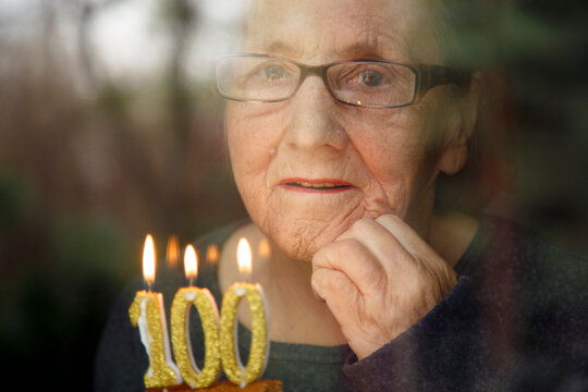 Portrait of an elderly woman with glasses holding anniversary candles.  An old woman holds a birthday cake alone on her centenary.