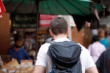 Fototapeta premium Male backpacker walking and exploring market, exploring stalls in local market, casual lifestyle in tropical market, rear view, at Yaowarat.