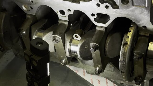 Mechanic in black gloves pointing at crankshaft inside engine block.