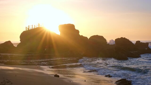 A scenic rock formation at Praia da Santa Cruz, Portugal. Waves crash on the beach as the sun sets, creating a beautiful view of nature.