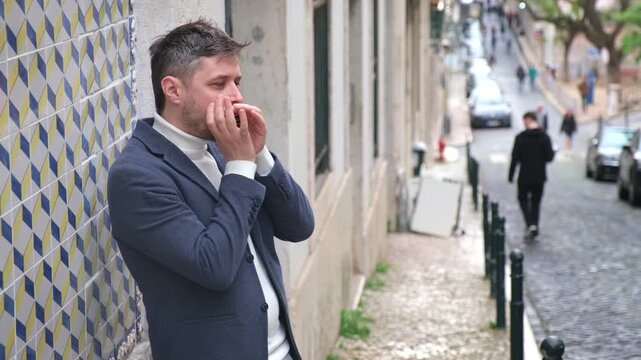 A man plays the harmonica on a busy street in a city in Portugal. People walk by as he performs music outdoors. The scene captures the lively atmosphere of urban life.