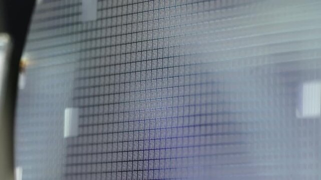 Macro view of a silicon wafer patterned with a precise grid of microchip dies, revealing photolithography detail and reflective surfaces from semiconductor manufacturing.