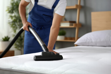 Fototapeta premium Man cleans mattress with vacuum in tidy bedroom