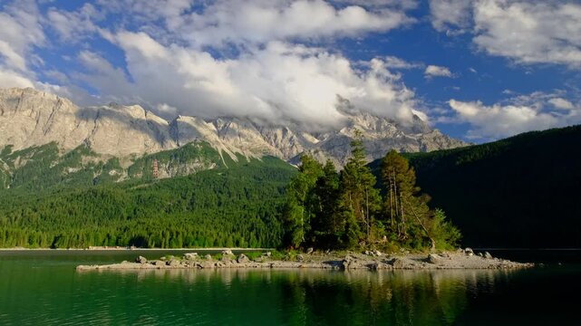 Video shot of a pine-covered island in Eibsee lake with the towering Zugspitze mountain range and clouds in the Bavarian Alps, Germany.