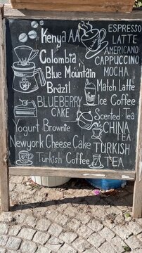 Chalkboard coffee menu features international coffee and dessert options on an outdoor sidewalk.