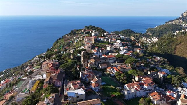 Aerial view of Ravello's terracotta rooftops cascading down the hillside towards the azure sea, nestled amongst lush greenery, Ravello, Campania, Italy.