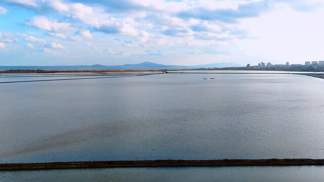 Wide view of salt pans and mountains on horizon. High angle shot of calm salt evaporation ponds with mountains in the far distance.