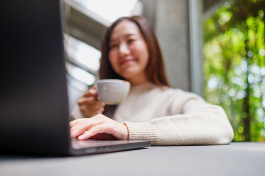 Blurred image of a woman working on laptop computer while drinking coffee in cafe