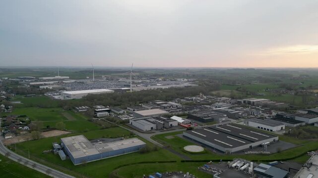 Aerial view of an industrial zone blending with nature, featuring modern buildings and wind turbines, showcasing a mix of green spaces and structures, Ath, Wallonia, Belgium.