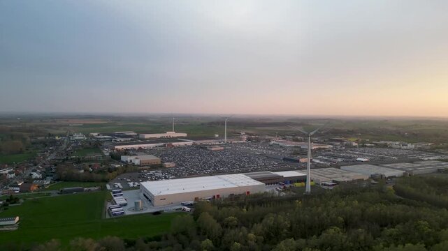 Aerial view of wind turbines towering over cars in parking lots, a modern industrial landscape with green spaces, Ath, Wallonia, Belgium.