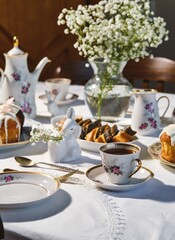 Fototapeta premium A spring Easter table setting with a vintage coffee set, Easter cupcakes, and a poppy seed roll on a white tablecloth. Happy Easter.