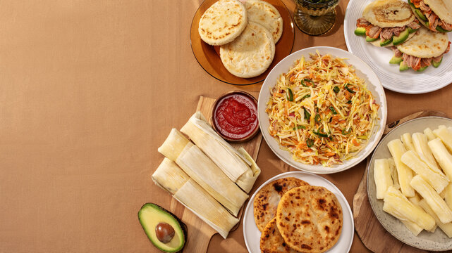 Flatlay border of Latin American dishes: pupusas, arepas, curtido, tajadas, humitas, yuca, copy space