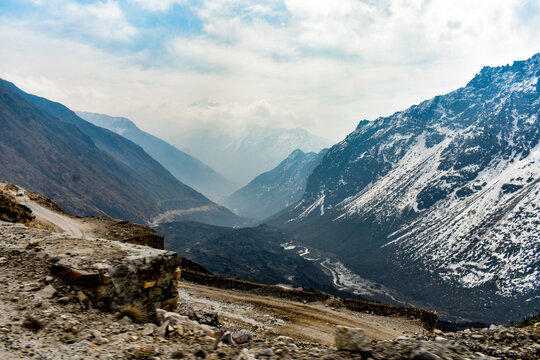 Remote mountain road with rocky snow-dusted Himalayan cliffs under overcast sky in North Sikkim.