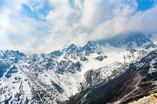 Snow-covered Himalayan peaks with clouds and winding mountain road, scenic high-altitude landscape in North Sikkim, India.