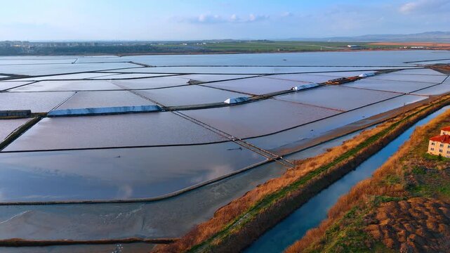 Aerial view of salt production basins with white salt heaps. Industrial landscape showing evaporation ponds and mounds of harvested salt.
