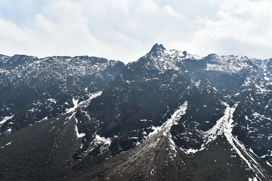 Rugged Himalayan mountain peaks with snow patches under cloudy sky, showcasing dramatic high altitude landscape in North Sikkim.