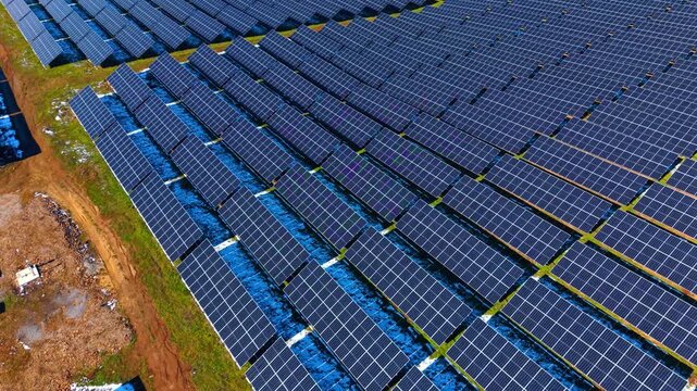 Angled aerial view of solar panel rows on hill. Photovoltaic modules arranged on a grassy slope with patches of snow. Sustainable energy production facility.