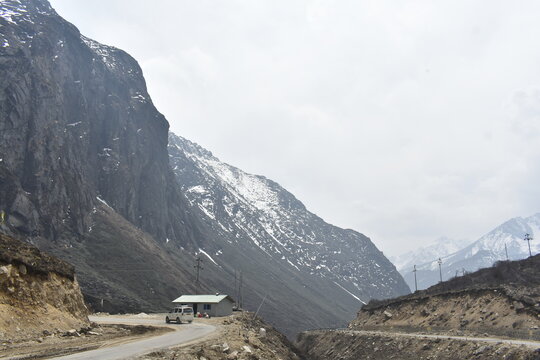Remote mountain road with rocky snow-dusted Himalayan cliffs under overcast sky in North Sikkim.