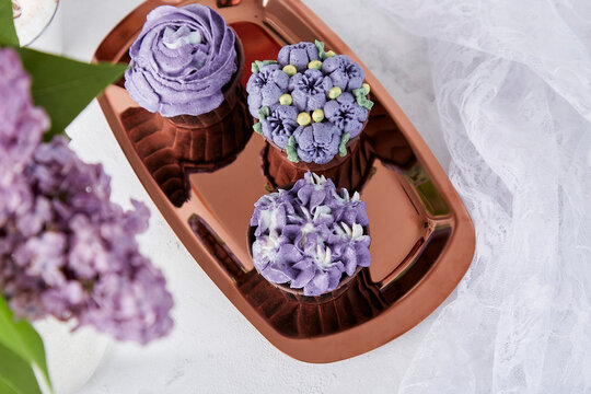 Purple french cupcakes on the golden tray. Desserts and lilac flowers flat lay.