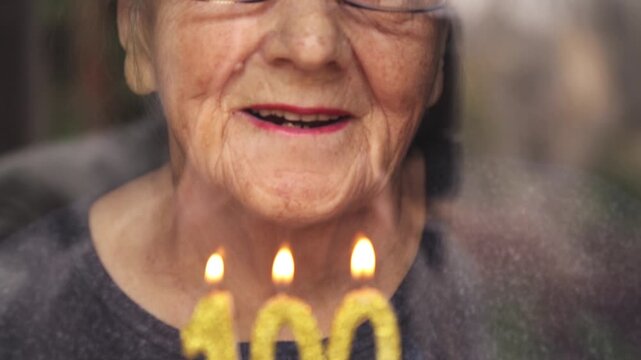 Portrait of an elderly woman with glasses holding anniversary candles.  An old woman holds a birthday cake alone on her centenary.