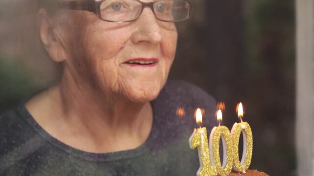 Portrait of an elderly woman with glasses holding anniversary candles.  An old woman holds a birthday cake alone on her centenary.