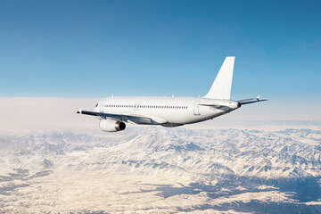 Obraz premium White modern airliner flies over snow covered mountains