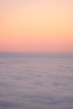 View of a serene, cloud-covered landscape under a gradient sky transitioning from soft orange to delicate pink, creating a dreamlike atmosphere, Teide National Park, Tenerife, Spain.