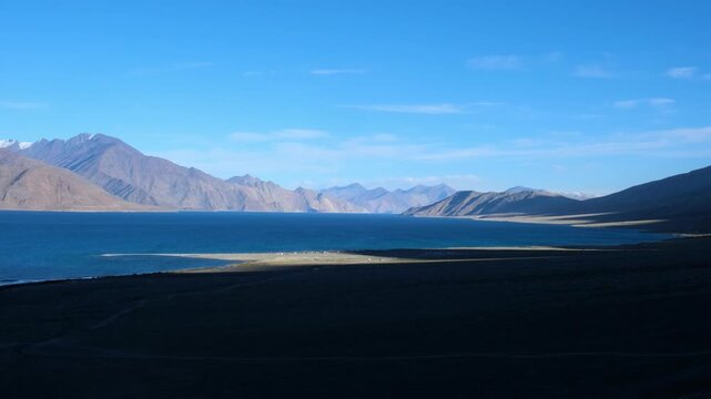 Cinematic shot of Pangong Lake during early morning, with soft golden light reflecting on the calm water as birds gently glide across the surface. Ideal moment for travel and nature storytelling.
