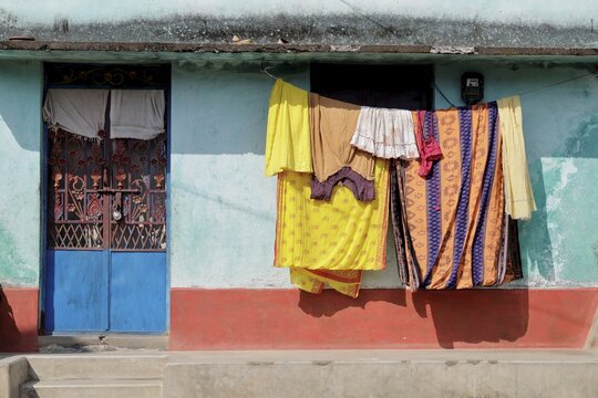 Odisha, India - 26 March 2026: View of a vibrant blue door contrasting with the soft teal walls, while laundry dries in the sun against the textured facade.