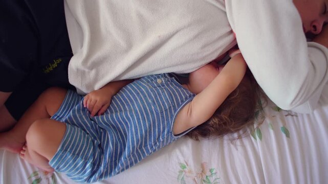Toddler lying beside sleeping mother reaching arm toward her face capturing intimate parent child closeness and quiet family moment in peaceful bedroom setting