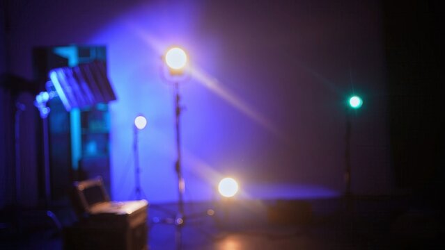 Blurred, defocused background with studio spotlights in a dark room with blue illumination. Concept of stage lighting, event production, concert design, media background, and entertainment technology.