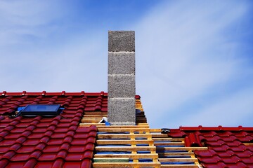 Budowa domu z elegancką dachówką i deskami z wierzby na dachu. Komin i zamontowane okno dachowe, słoneczna pogoda. © Adam