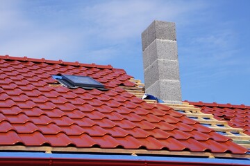 Budowa domu z elegancką dachówką, deski z wierzby na dachu, komin już zamontowany, słoneczne niebo nad budową © Adam