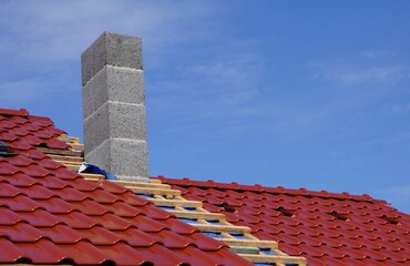 Solidny komin, dachówka i trwające prace dekarskie. Montaż komina i budowa stawianie dachówki na dachu. © Adam