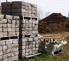 Wysoko poukładane bloczki budowlane, obok paleta, w tle usypana ziemia na placu budowy, błotnista droga dojazdowa. © Adam