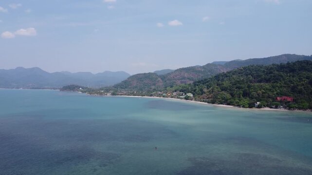 Smooth aerial drone footage flying above Ko Man Nai island near Koh Chang, Thailand. Crystal clear blue waters surround lush green jungle and quiet beaches, showcasing untouched tropical beauty.