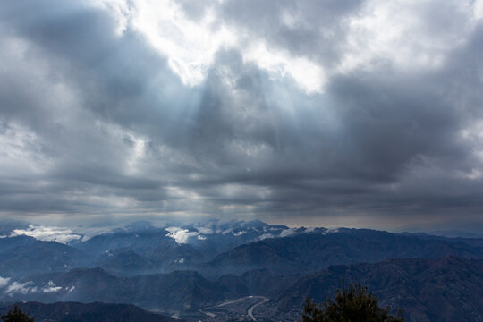 View of sunlight piercing through the dark, ominous clouds blanketing the rugged mountain range and winding river below, Muzaffarabad, Azad Kashmir, Pakistan.